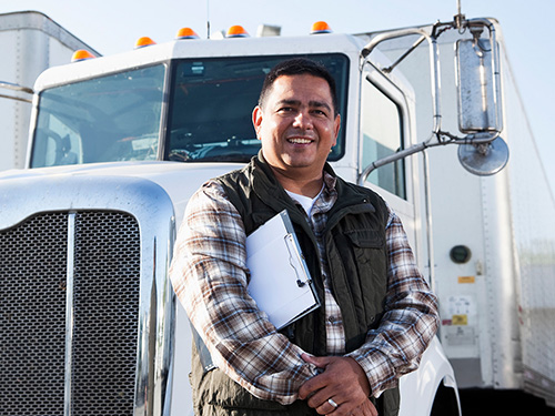 Hispanic truck driver (40s) standing in front of semi-truck with clipboard.